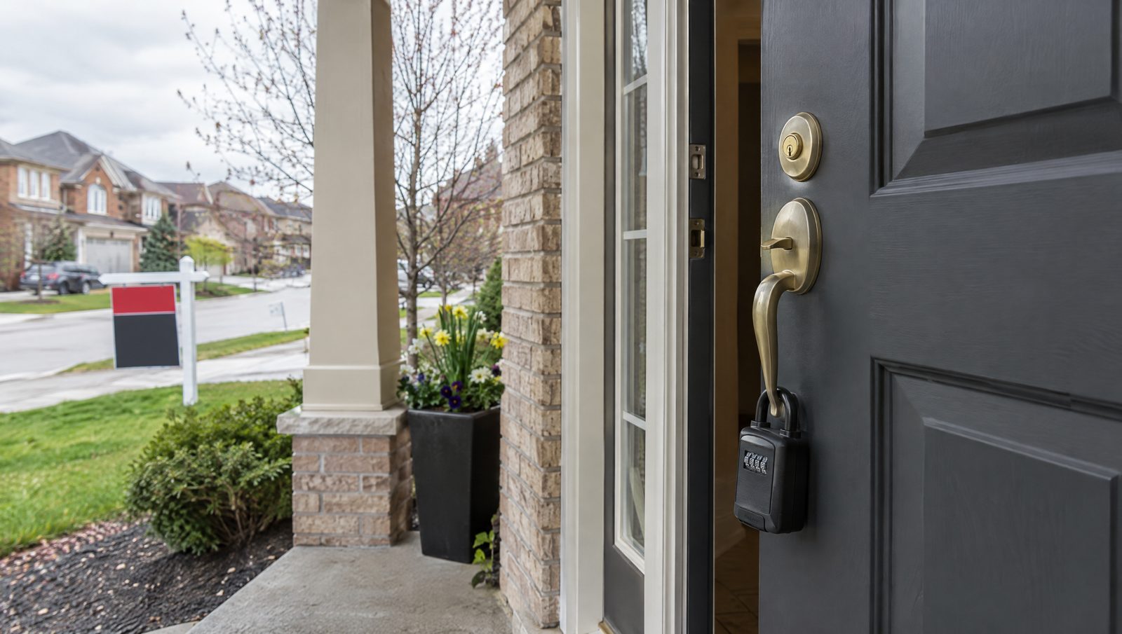 A charcoal front door in Springdale, Brampton, slightly open with a lockbox on the handle