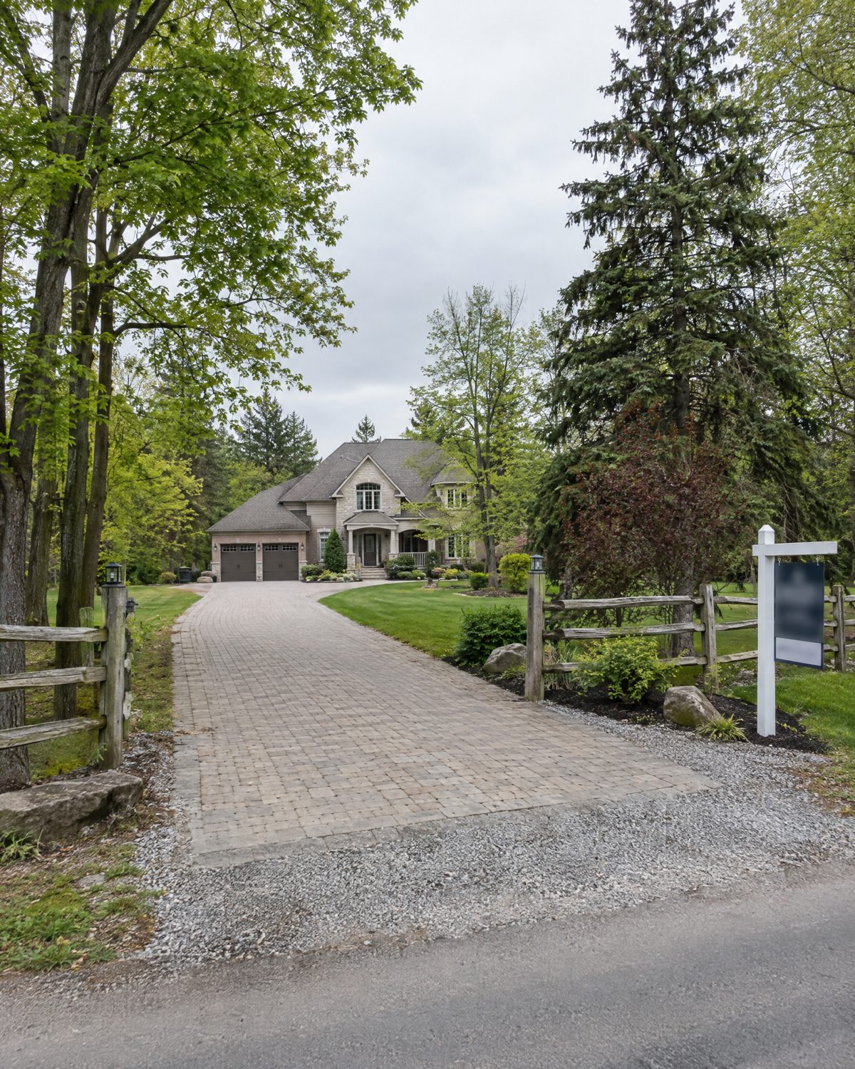Long gravel and interlock drive to a Kleinburg estate lot house with a cedar fence and a sold sign at the road